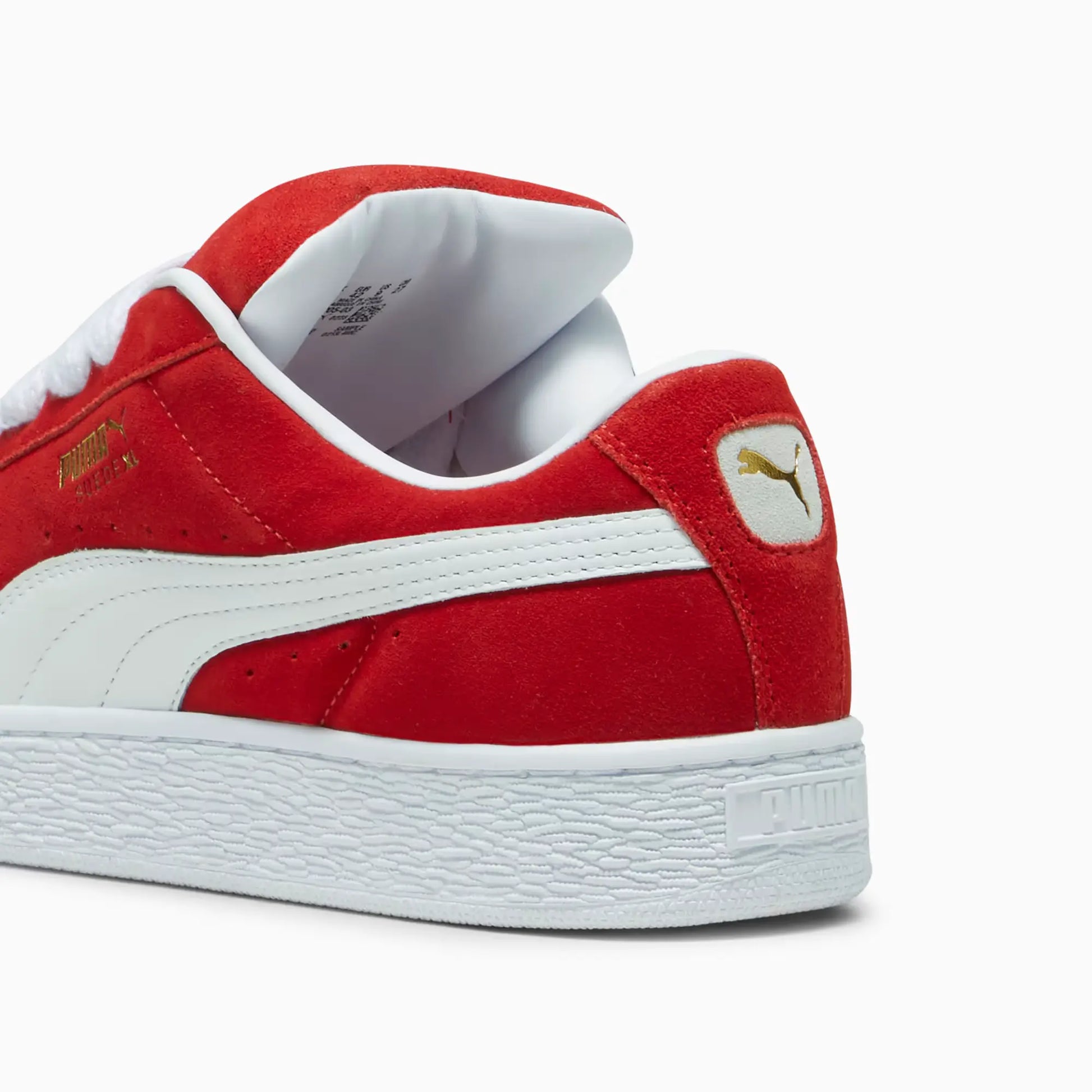 Close-up of the red suede Puma Suede XL sneakers, showcasing gold Puma logo on the side and heel with white rubber sole.