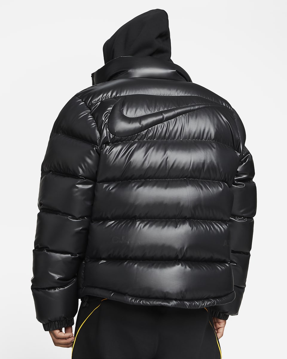 A Black Nike Nocta Puffer Jacket worn by a model facing away and displaying the back with the nike swoosh pointing to the right.